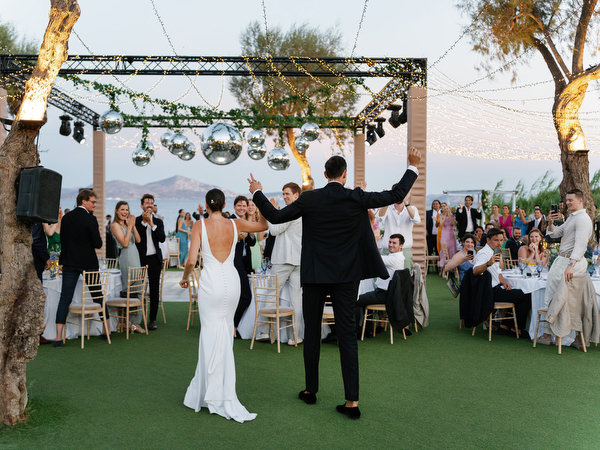 Bride and groom walking under white arch at Island Resort, luxury Athens Riviera destination wedding.