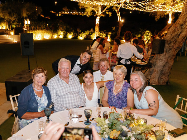Family seated at reception at Island Resort, elegant Athens Riviera seaside wedding at night.