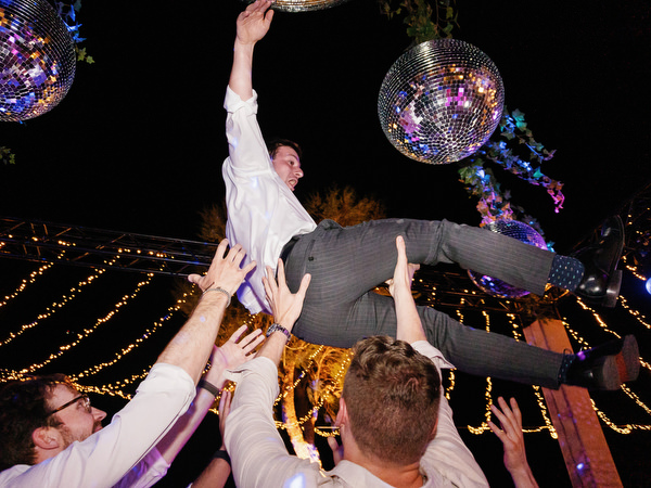 Guest lifted during dance celebration at Island Resort, lively Athens Riviera Jewish wedding tradition.