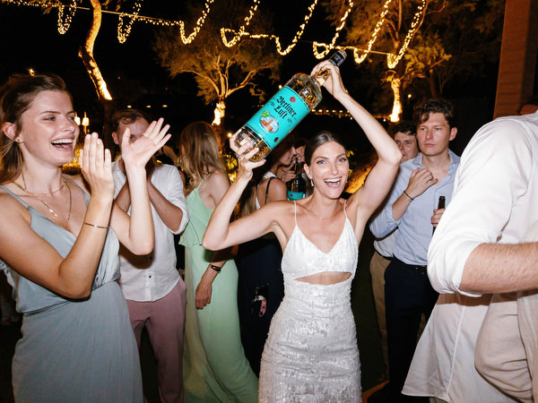 Bride dancing under string lights at Island Resort, vibrant Athens Riviera seaside wedding party.