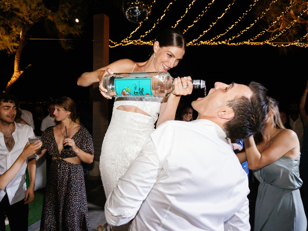 Bride pouring at Groom a celebratory drink on the dance floor at Island Resort, lively Athens Riviera Jewish wedding reception.