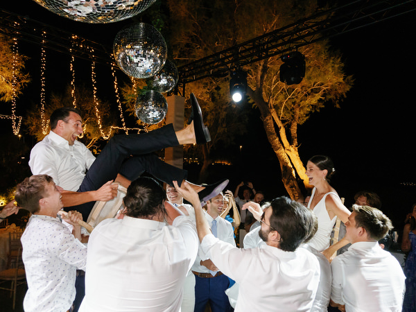 Groom celebrating mid-air at Island Resort wedding party, lively Athens Riviera night reception.