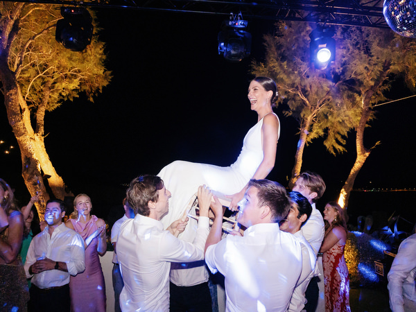 Bride lifted during the hora at Island Resort, energetic Athens Riviera Jewish wedding celebration.