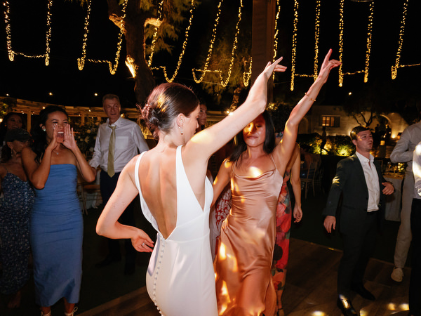 Bride dancing under string lights at Island Resort, luxury Athens Riviera wedding celebration.
