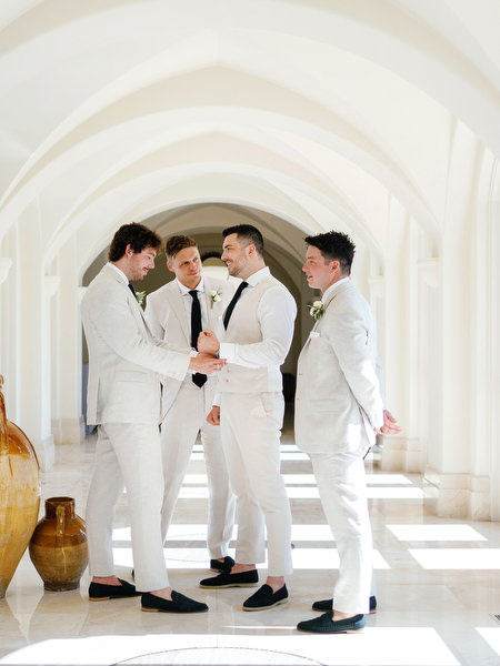 Groom and groomsmen in light suits inside white arched hallway at Anassa Hotel Cyprus.