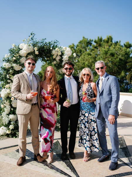 Wedding guests posing beside white floral arch at Anassa Hotel Cyprus ceremony.