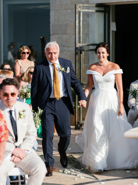 Bride walking down aisle with father at Anassa Hotel coastal wedding in Cyprus.