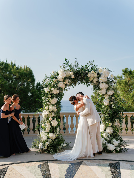 Bride and groom kissing under white floral arch at Anassa Hotel Cyprus.