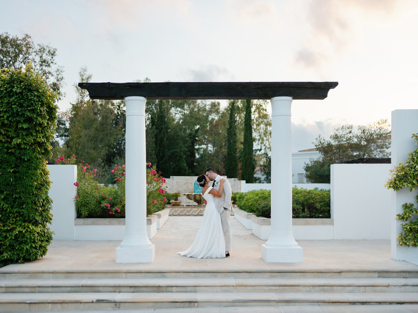 Bride and groom kissing beneath white pergola at Anassa Hotel Cyprus wedding.