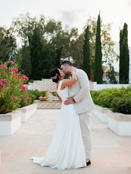Bride and groom embracing in Mediterranean gardens at Anassa Hotel.