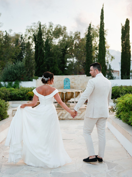 Bride and groom walking hand in hand through Anassa Hotel courtyard.
