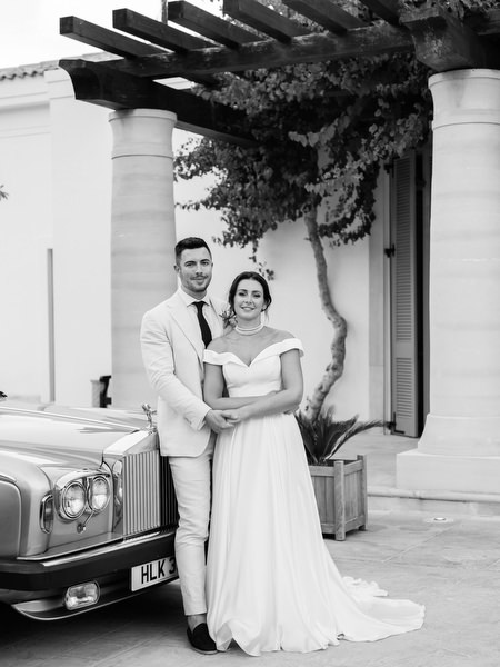 Bride and groom posing beside vintage rolls royce at Anassa Hotel wedding.