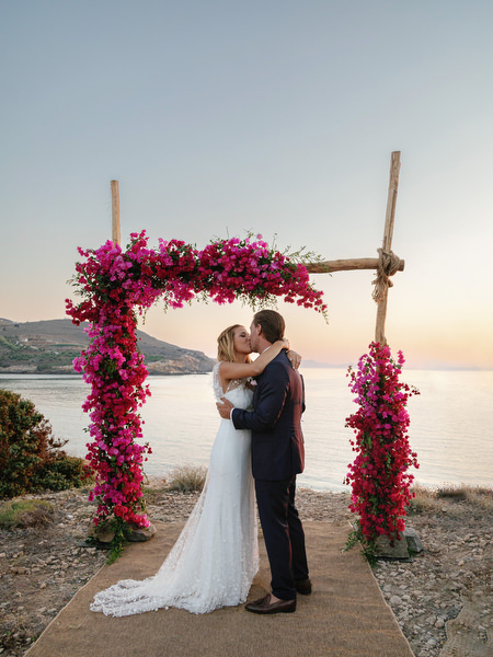 Bride and groom kissing under pink bougainvillea arch in Antiparos.