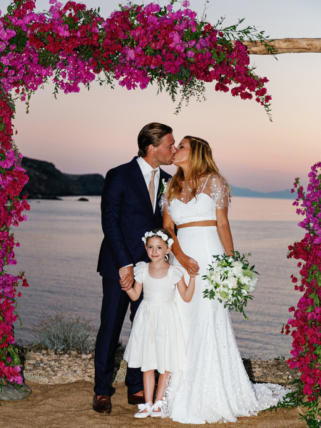 Bride and groom kissing under bougainvillea arch in Antiparos at sunset.