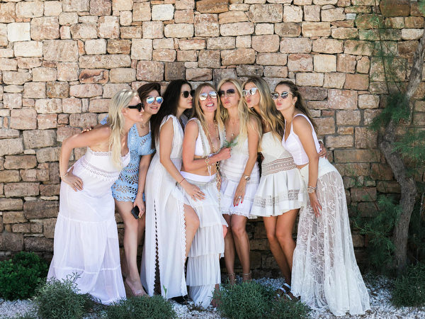 Bride and friends posing playfully against stone wall during wedding weekend brunch