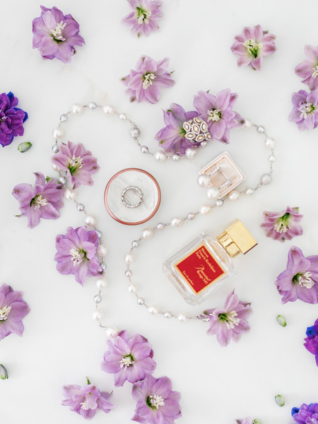 Bridal accessories including pearl necklace and perfume styled with purple florals for an Athens Riviera wedding at Four Seasons Astir Palace