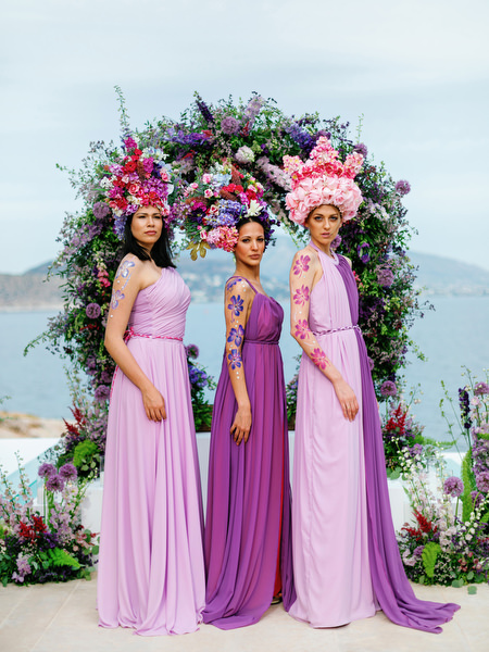 High-fashion guests in lilac gowns posing beneath a floral arch at an Island Resort Athens Riviera wedding on the Athens Riviera