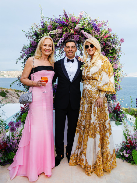 Wedding guests in pink and gold gowns posing by the sea at a refined Athens Riviera wedding at Island Resort Athens Riviera