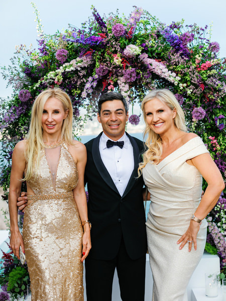 Elegant guests posing with groom beneath a lush floral arch at an Island Resort Athens Riviera wedding overlooking the Athens Riviera