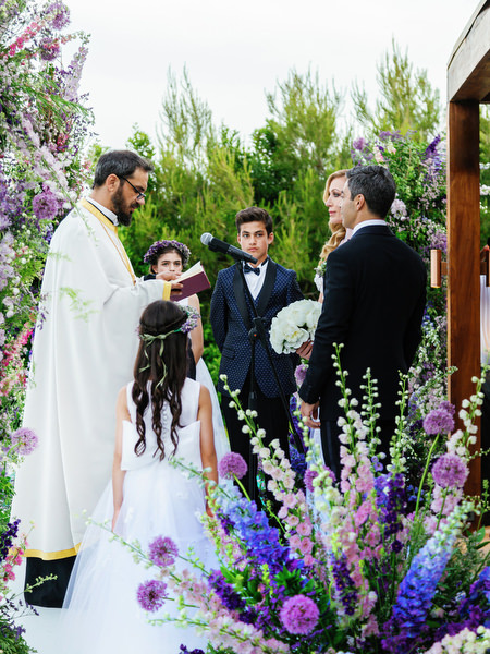 Priest officiating seaside ceremony framed by purple florals at an Athens Riviera wedding at Island Resort Athens Riviera