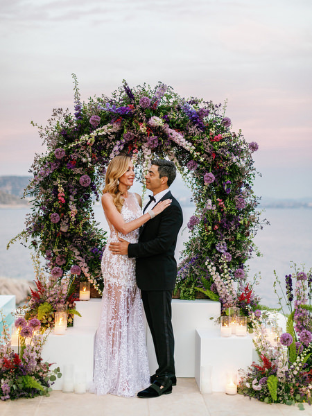 Romantic sunset portrait of the couple beneath a floral arch during their Athens wedding at Island Resort Athens Riviera