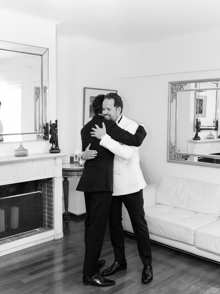 Groom hugging a family member during black-tie wedding preparations in Athens
