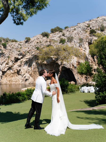 Bride and groom sharing a kiss with dramatic cliffs of Vouliagmeni Lake in background