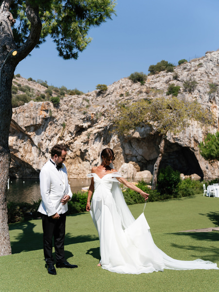 Bride showing flowing train to groom during first look at Vouliagmeni Lake wedding