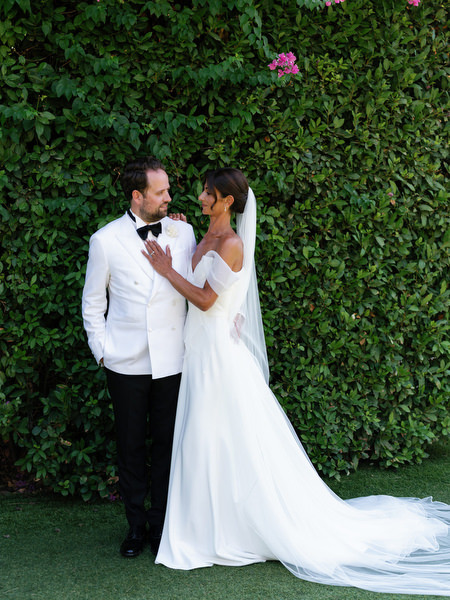 Bride and groom posing against lush green hedge at Lake Vouliagmeni Athenian Riviera