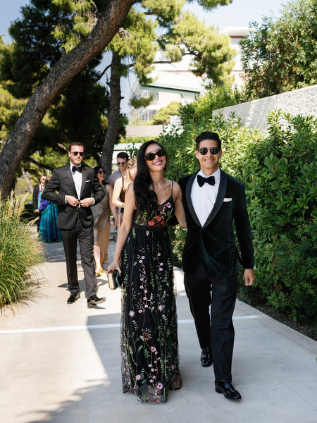 Elegant wedding guests in formal attire walking along garden path on the Athenian Riviera