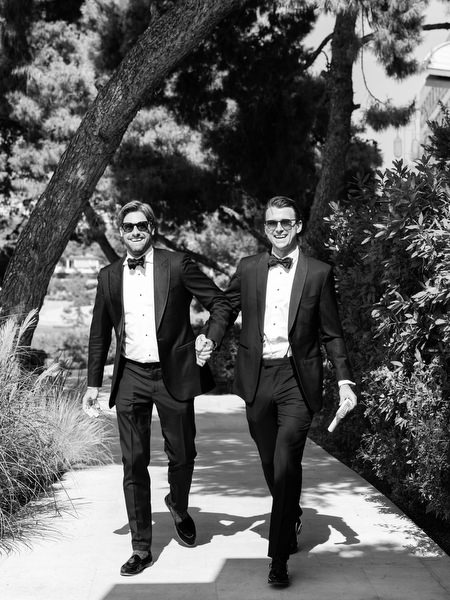 Groomsmen in classic black tuxedos walking through garden at Four Seasons Astir Palace Athens