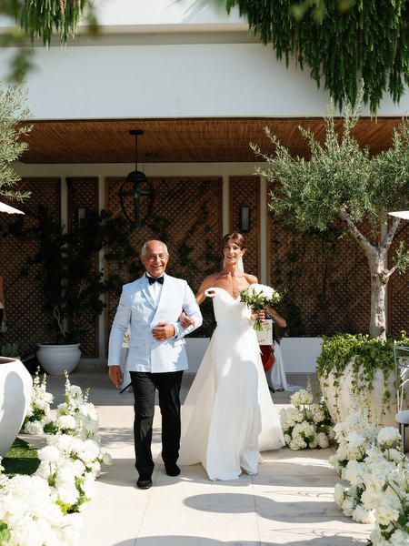Bride walking arm-in-arm with her father toward lakeside ceremony at Four Seasons Astir Palace Athens