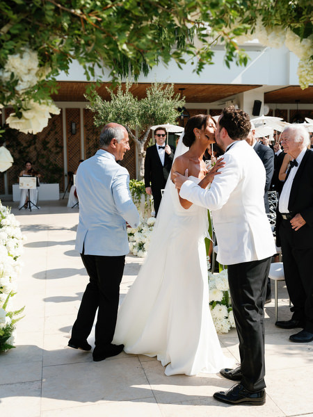 Bride embracing her groom moments before lakeside ceremony at Four Seasons Astir Palace Athens