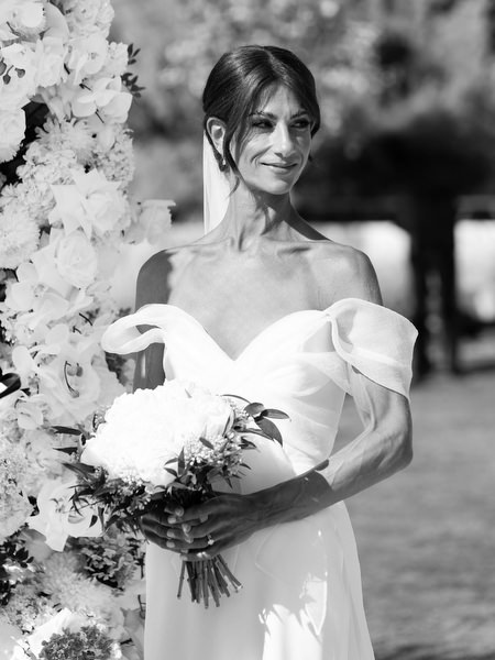 Bride holding white bouquet beside lush ceremony flowers at Vouliagmeni Lake