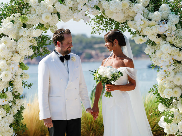 Bride and groom sharing first kiss under white floral arch at Four Seasons Athens