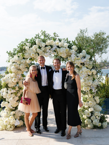 Family members in formal attire posing beneath white roses arch at Four Seasons Athens