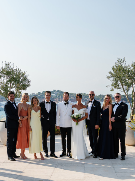 Bride and groom posing with wedding party in black-tie attire overlooking the Athenian Riviera