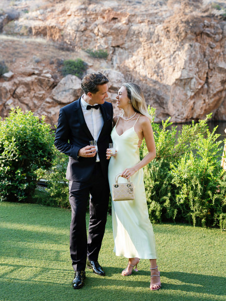Well-dressed guests walking across lawn during black-tie wedding at Vouliagmeni Lake