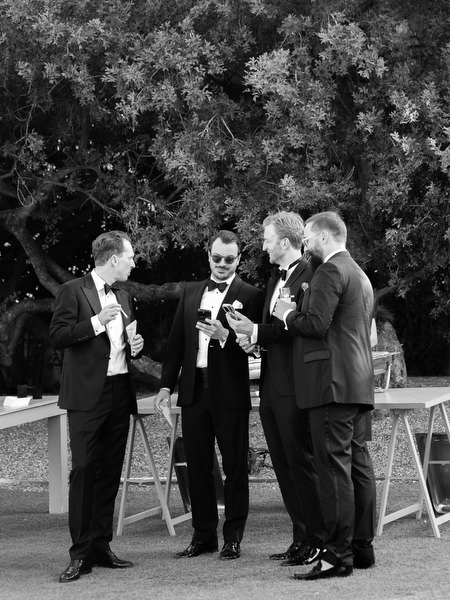 Group of groomsmen sharing drinks beneath trees at Athens destination wedding