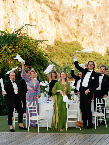 Guests standing and waving white napkins during joyful lakeside wedding party