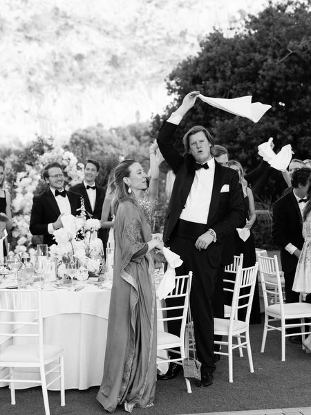 Black-tie guests cheering and waving napkins during lively wedding reception entrance