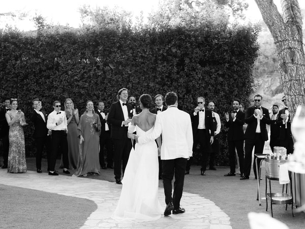 Bride and groom standing outdoors surrounded by guests at elegant lakeside reception