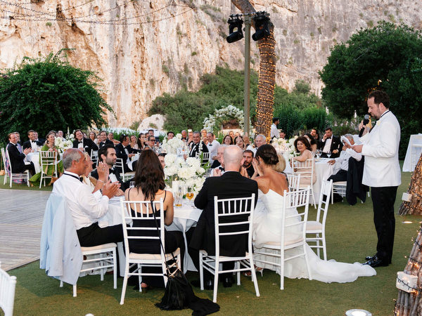 Groom in white dinner jacket delivering heartfelt speech at lakeside reception