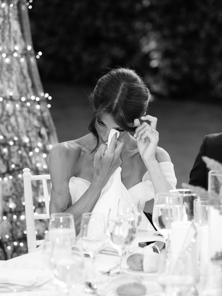 Bride emotional and dabbing her eyes while seated at reception table