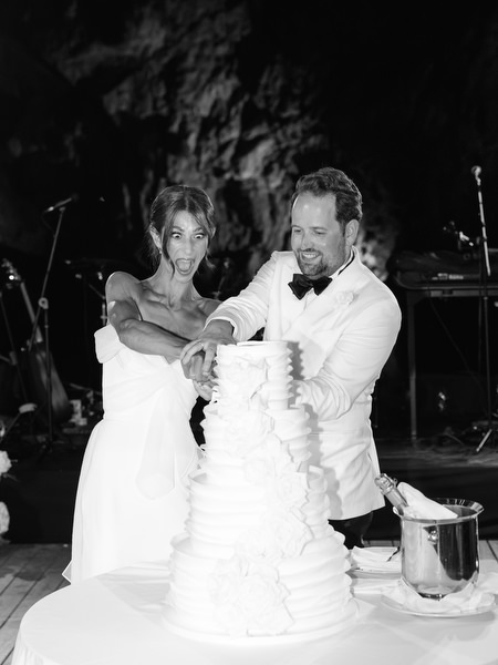 Bride and groom smiling while cutting wedding cake at night reception