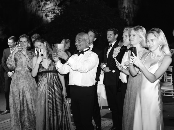 Elegant wedding guests clapping and capturing moment on phones during evening celebration