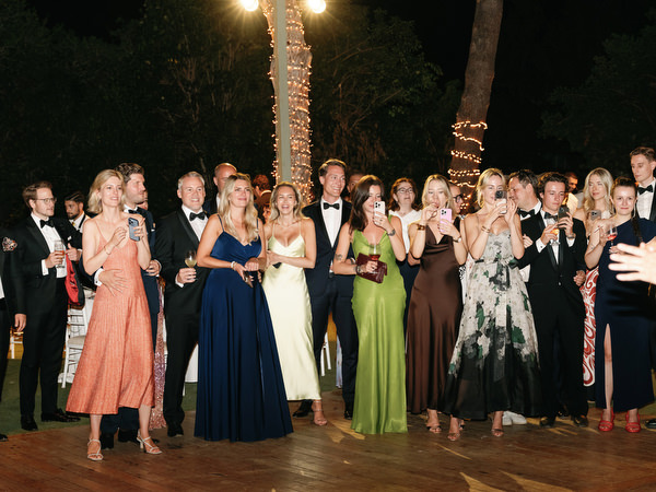 Black-tie guests gathered on outdoor dance floor under string lights at lakeside wedding