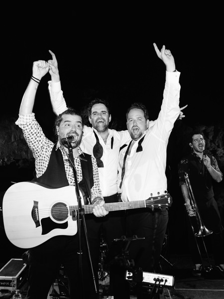 Wedding band singing and playing guitar while guests cheer with hands raised
