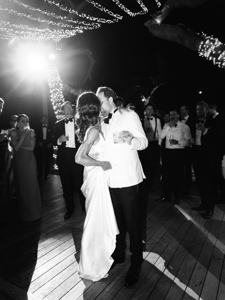 Bride and groom dancing closely under dramatic backlighting at lakeside reception