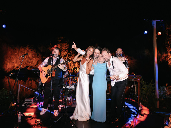 Bride and friends singing on stage with live band during high-energy lakeside wedding party
